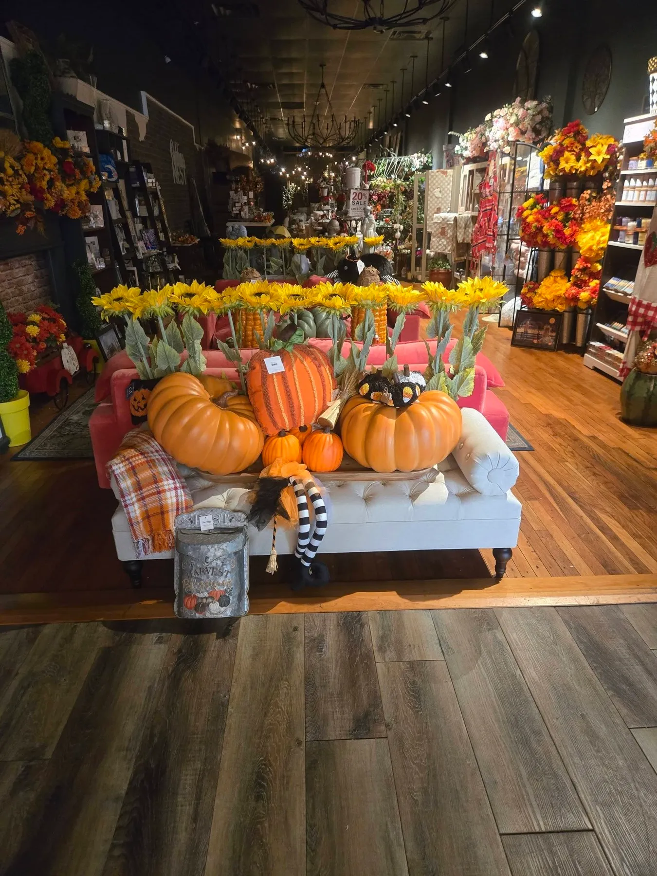 The shop floor: a white tufted sofa piled with pumpkins, sunflowers overhead, and shelves beyond