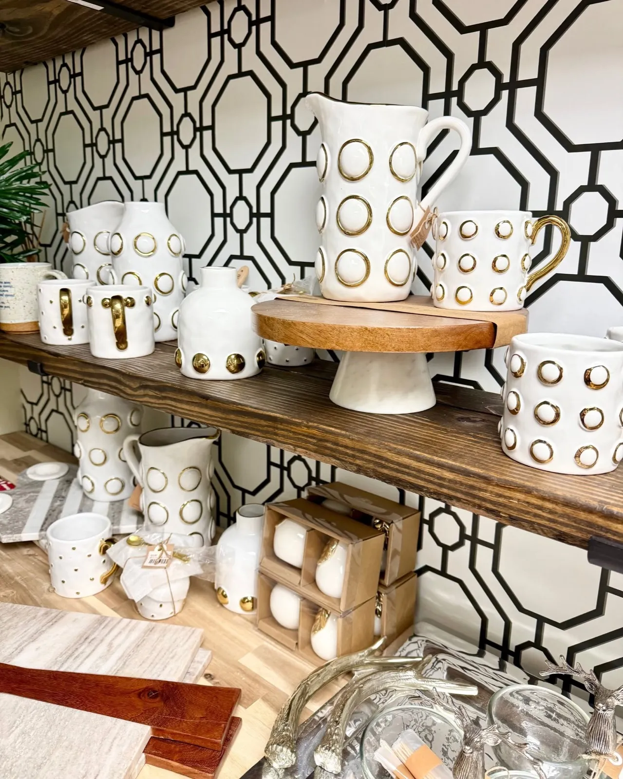 White stoneware pitchers and mugs ringed with raised gold dots on a wood shelf